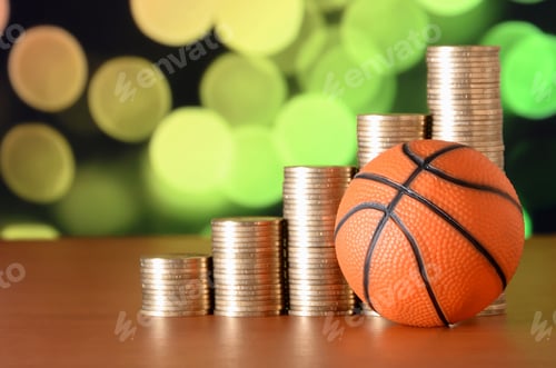 Preview: Basketball and stacks of golden coins in growth graph on the blurred bokeh background