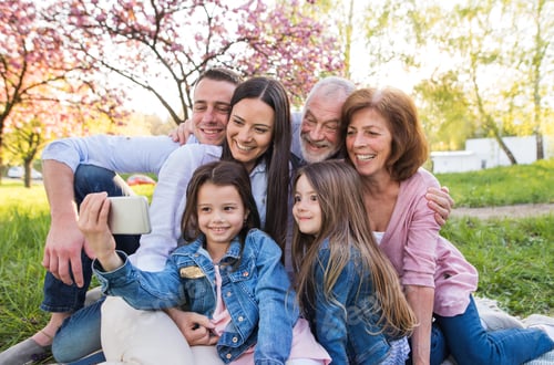 Preview: Three generation family sitting outside in spring nature, taking selfie
