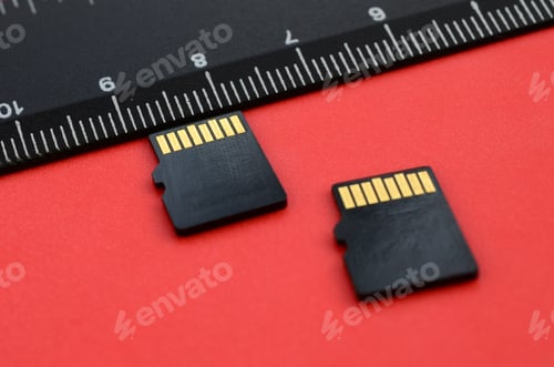 Preview: Two small micro SD memory cards lie on a red background next to a black ruler