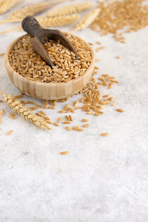 Preview: Bowl of raw dry rye grain with a wooden spoon on white table close up, copy space