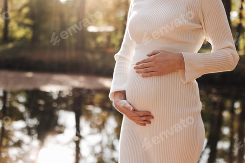 Preview: Mothers day. Beautiful young pregnant woman in white tight knit dress with little belly relaxing