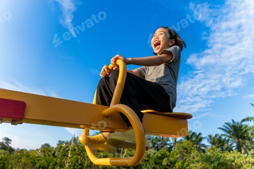Preview: A happy young Asian girl on a yellow seesaw.