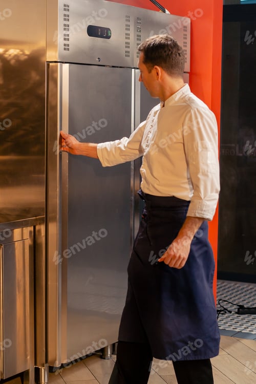 Preview: professional kitchen chef open the fridge and chooses ingredients for cooking food concept