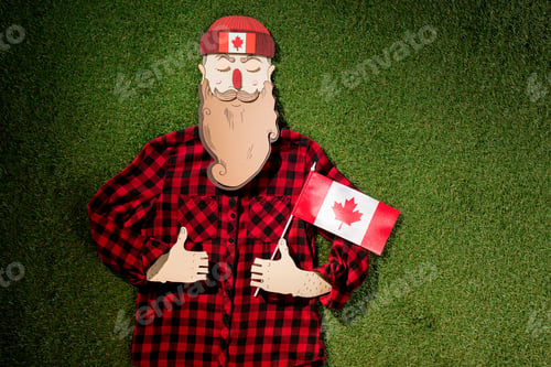 Preview: cardboard man in plaid shirt holding canadian flag and showing thumbs up signs on green grass