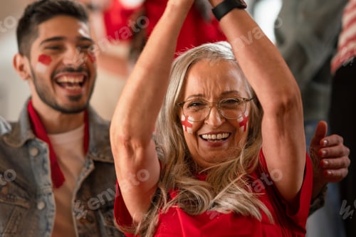 Preview: Excited senior woman football fan supproting English national team in live soccer match at stadium.