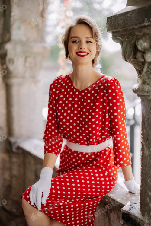 Preview: Smiling woman wearing red polka dot dress and white gloves posing on balcony