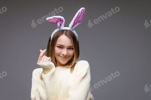 Preview: smiling young girl with bunny ears shows a mini heart with fingers