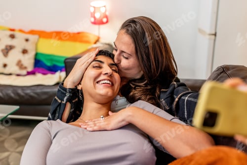 Preview: Happy lesbian couple taking a selfie while relaxing on the couch