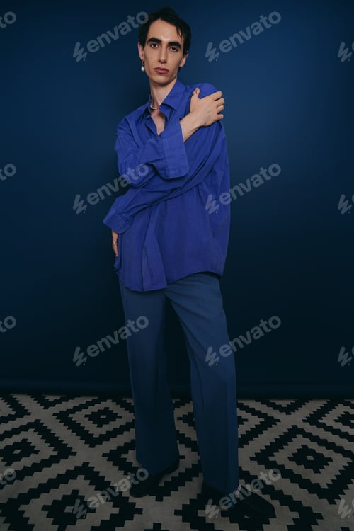 Preview: Stylish man poses confidently against a vibrant blue backdrop, showcasing modern fashion trends