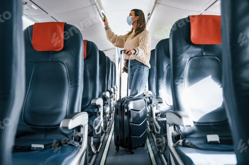 Preview: With lugagge. Young female passanger in casual clothes is in the plane