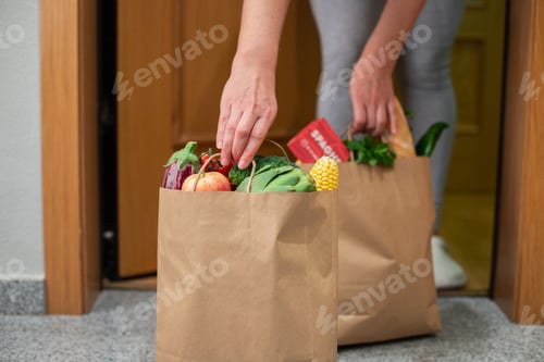 Preview: A woman picks up a bag of food at the door of her house.