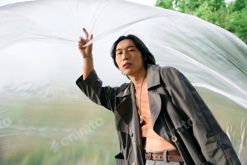 Preview: Stylish young man in grey trench coat enjoys a moment in the park surrounded by nature
