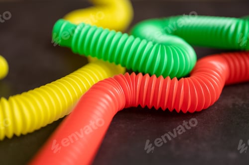 Preview: kids colorful anti stress sensory pop tube plastic fidget push toy on a black table or floor