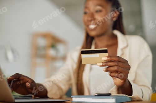 Preview: Close-up of black woman using credit card while home shopping over laptop.