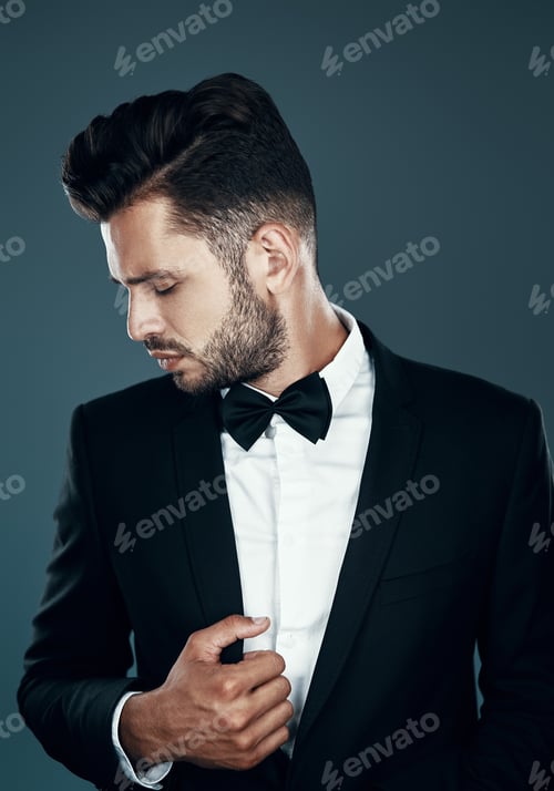 Preview: Charming young man in bow tie adjusting jacket while standing against grey background