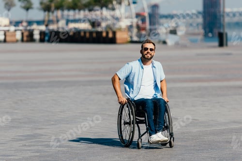 Preview: smiling handsome man in sunglasses using wheelchair on street