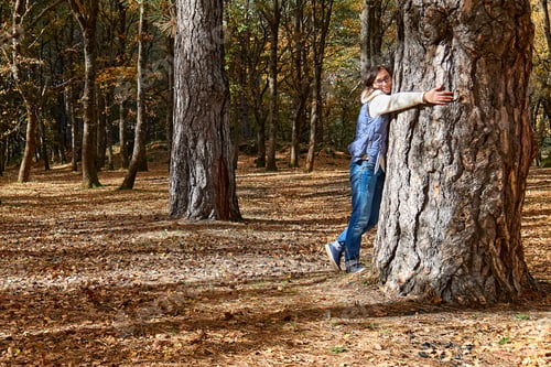 Preview: Happy woman hugging big tree in autumn forest.