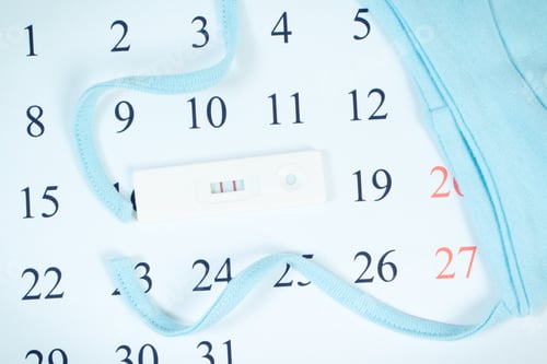 Preview: Pregnancy test with positive result and cap for newborn on calendar, expecting for baby