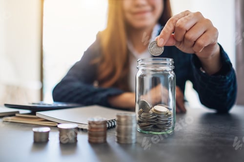 Preview: Woman Saving Money in Glass Jar at Desk