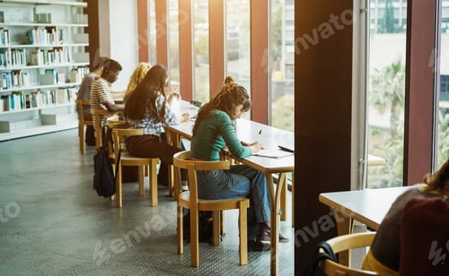 Preview: Young group of students studying together inside university library - Focus on center girl hand