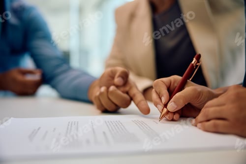 Preview: Close up of bank manager closing deal with a couple and pointing at place of signature on document.