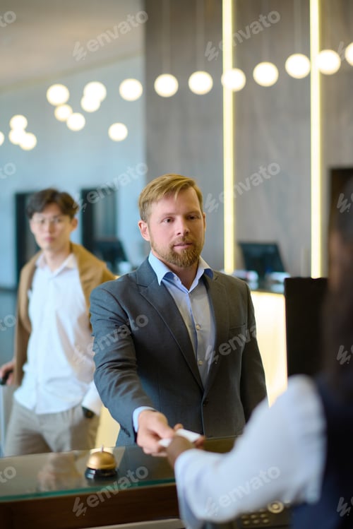 Preview: Confident businessman in formalwear taking keycard held by receptionist