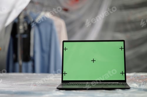 Preview: Laptop with Green Mockup Screen on Table Covered with Film in Fashion Art Studio