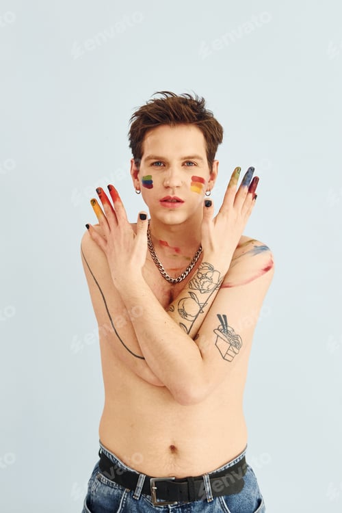 Preview: Young gay man is standing in the studio and posing for a camera. Shirtless guy with rainbow make up