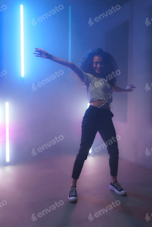 Preview: Modern dance girl dancer dancing in neon light doing gymnastic exercises in studio, copy space.