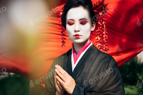 Preview: selective focus of tree branches and beautiful geisha with greeting gesture and red cloth on