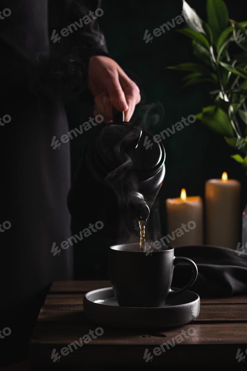 Preview: Woman in black pouring hot tea or coffee into a cup