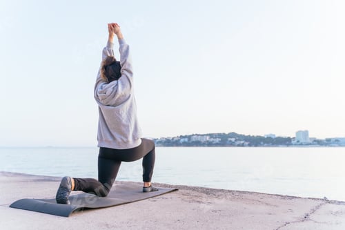 Preview: Young caucasian woman doing yoga exercises and stretching at sunset on a mat by the sea