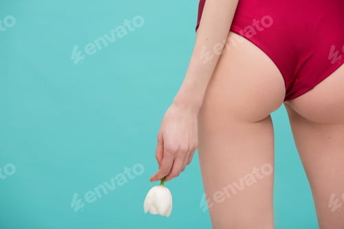 Preview: Beautiful sexy buttocks in red swimsuit and hand with white tulip flower over mint color background