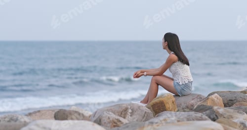 Preview: Woman sitting at seaside and looking at the sea