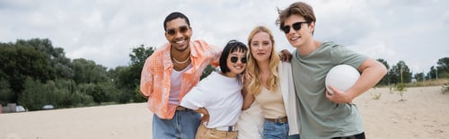 Preview: young and happy interracial friends with ball smiling at camera on beach, banner