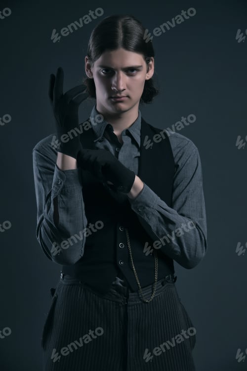 Preview: Mysterious Western 1900 Fashion Man With Brown Hair Wearing Gloves. Studio Shot Against Grey.