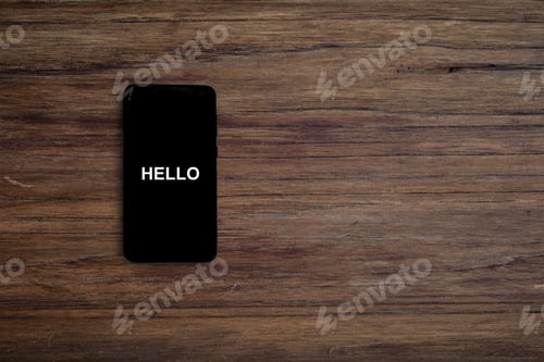 Preview: Turned on black phone displaying hello on wood desk background.
