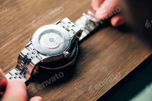 Preview: Selective focus of watchmaler holding wristwatch on stand on wooden table