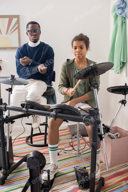 Preview: Cute schoolgirl hitting cymbal of drumkit during home repetition