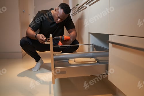 Preview: Diligent man screwing in drawer handle with drill