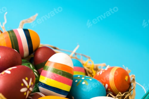 Preview: Colorful easter eggs resting in a nest on a vibrant blue backdrop