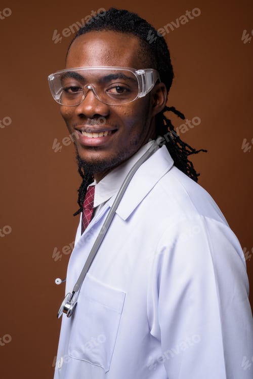 Preview: Young handsome African man doctor wearing protective glasses aga