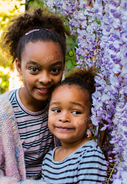 Preview: Portrait of two siblings girls of mixed race standing in front of purple wisteria flowers family