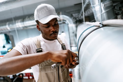 Preview: Man works on industrial pipe maintenance in a large workshop during the day