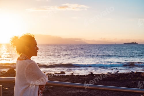 Preview: Side view of young adult woman admiring and enjoying golden sunset at the beach