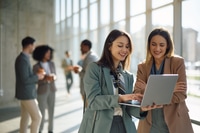 Preview: Happy businesswomen using laptop in a hallway of an office building.