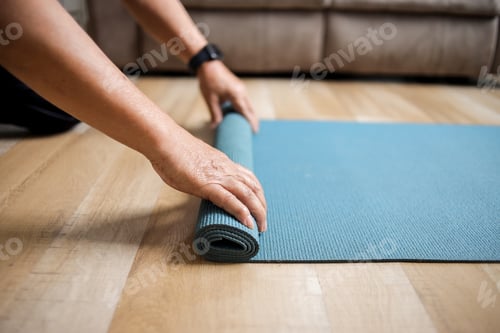 Preview: Side view of a person rolling up a blue mat at floor, preparing for yoga practice