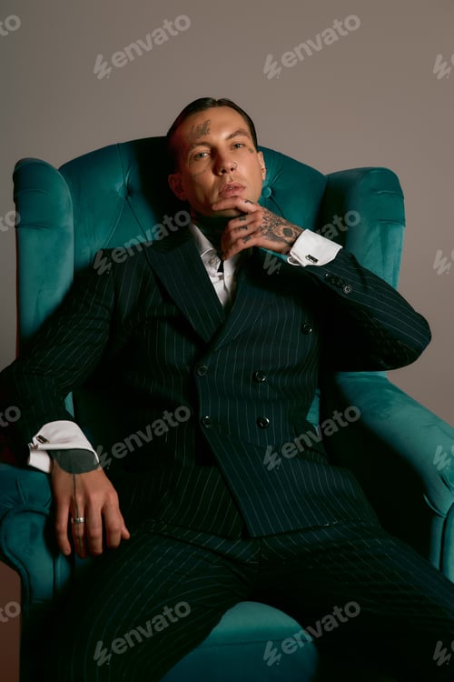 Preview: Stylish young man resting confidently in an elegant armchair with a striking pose