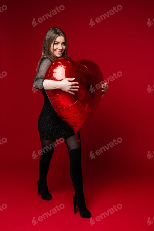 Preview: Smiling pretty woman hugging red balloon in studio