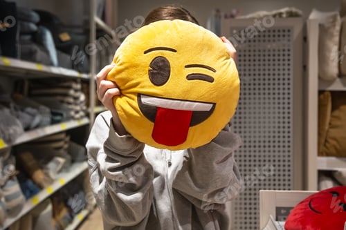 Preview: Young woman holding a smiley pillow in her hands in a store.